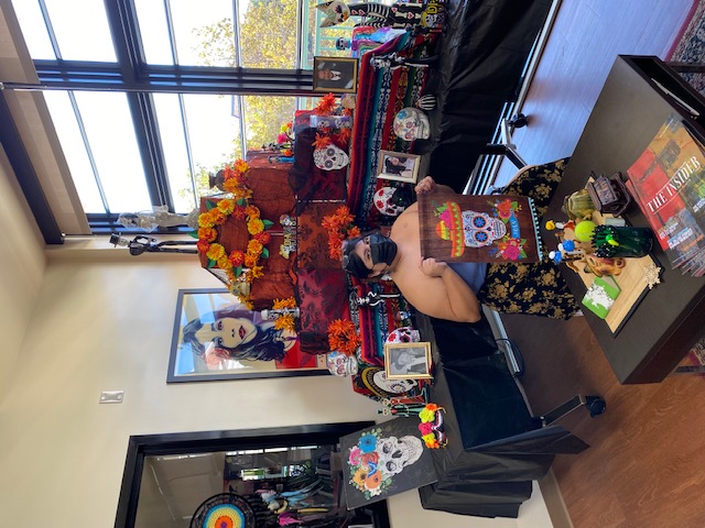 Student holding up skull decoration in front of ofrenda (altar)